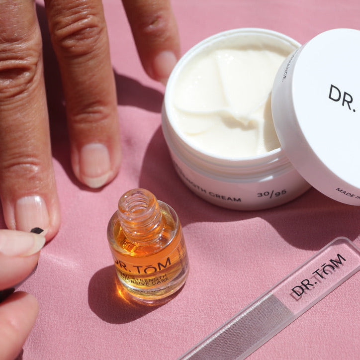 Dr. Tom skincare products including a jar, dropper, and strip on a pink background