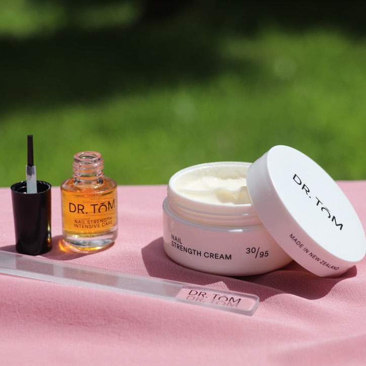 Dr. Tom skincare products on a pink surface with a blurred green background